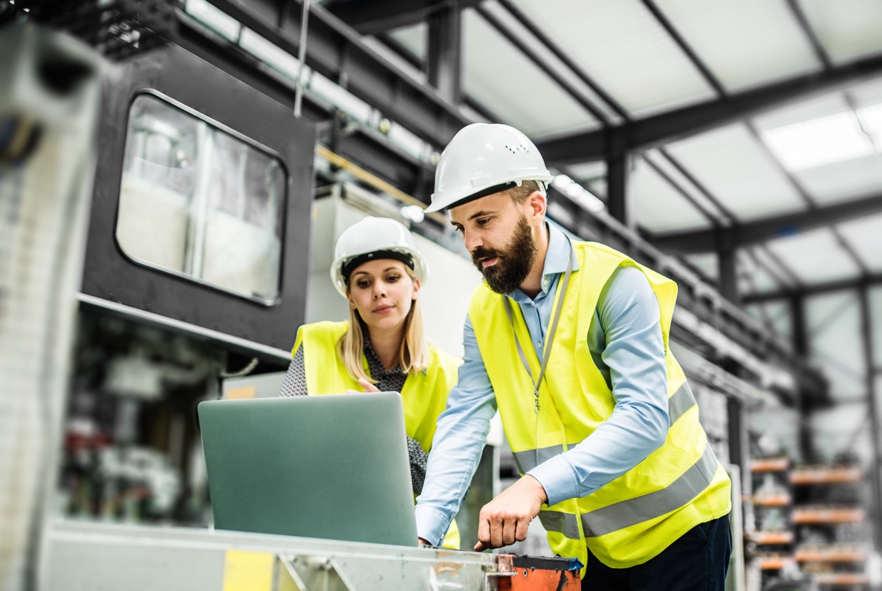 A portrait of an industrial man and woman engineer with laptop in a factory, working.